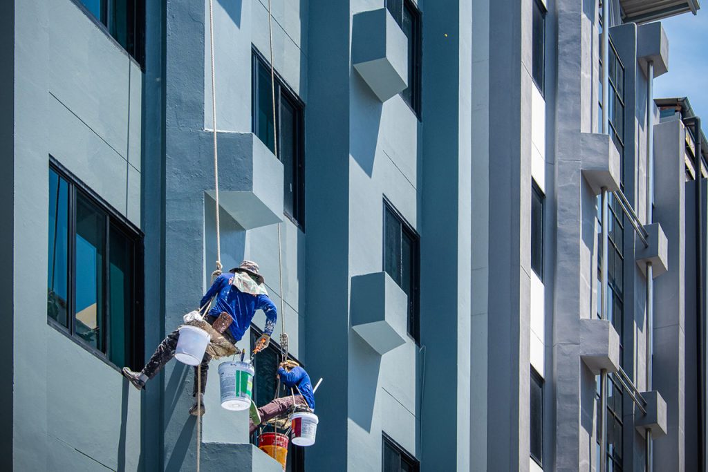 2 painters are hanging on ropes and harnesses paint the exterior of building.